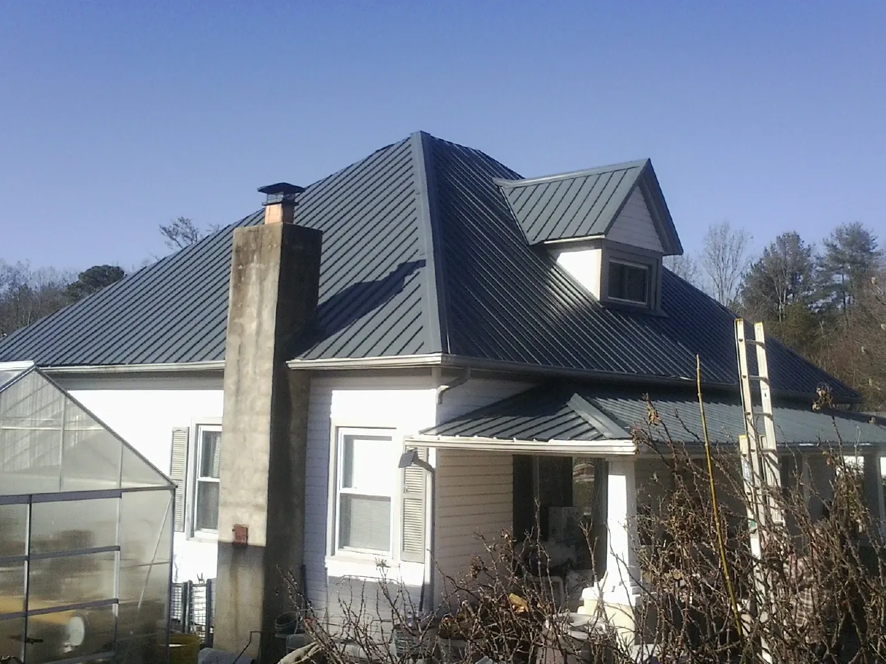 Dark blue standing seam metal roof on a white farmhouse with dormer — Slate & Tile Roof Repair by Roofing Brothers in Pinola