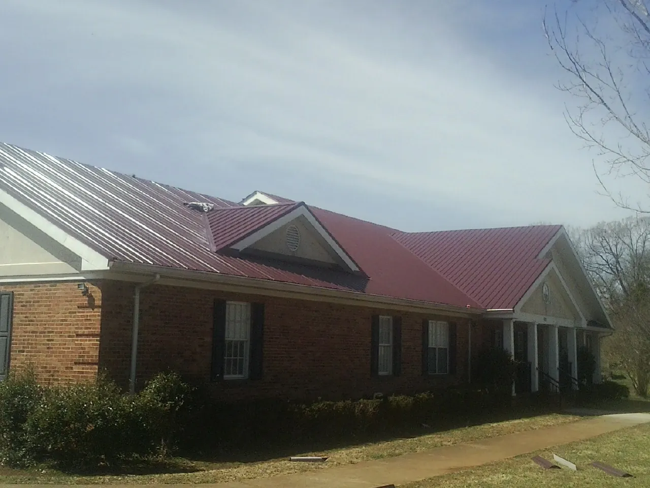 Red metal roof with gabled entries on a long brick building, from a Hail Damage Roof Repair job in Pinola