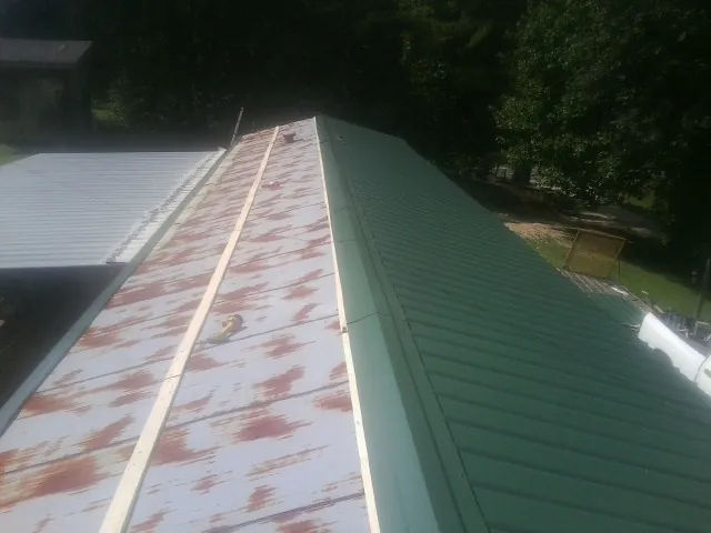 Old rusted panels beside newly installed green metal roofing — Wind Damage Roof Repair by Roofing Brothers in Pinola