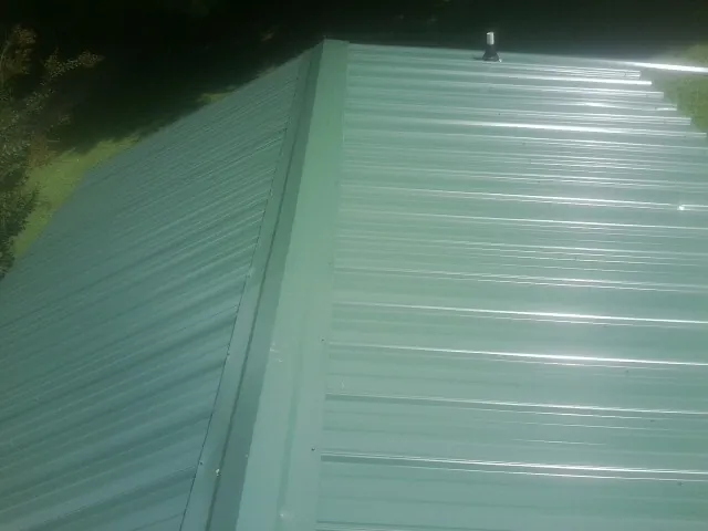 New green metal panels meeting at the ridge of a roof — Flat Roof Repair work by our crew in Pinola