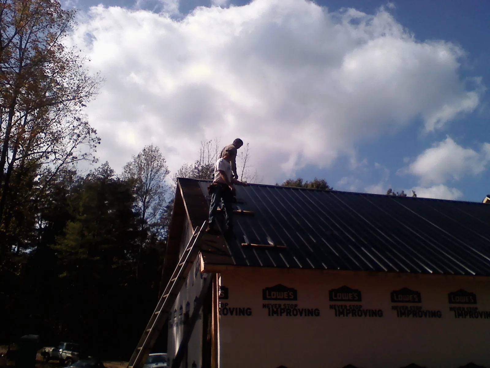 Roofer fastening dark metal panels high against a cloudy sky, from a Roof Inspection job in Pinola