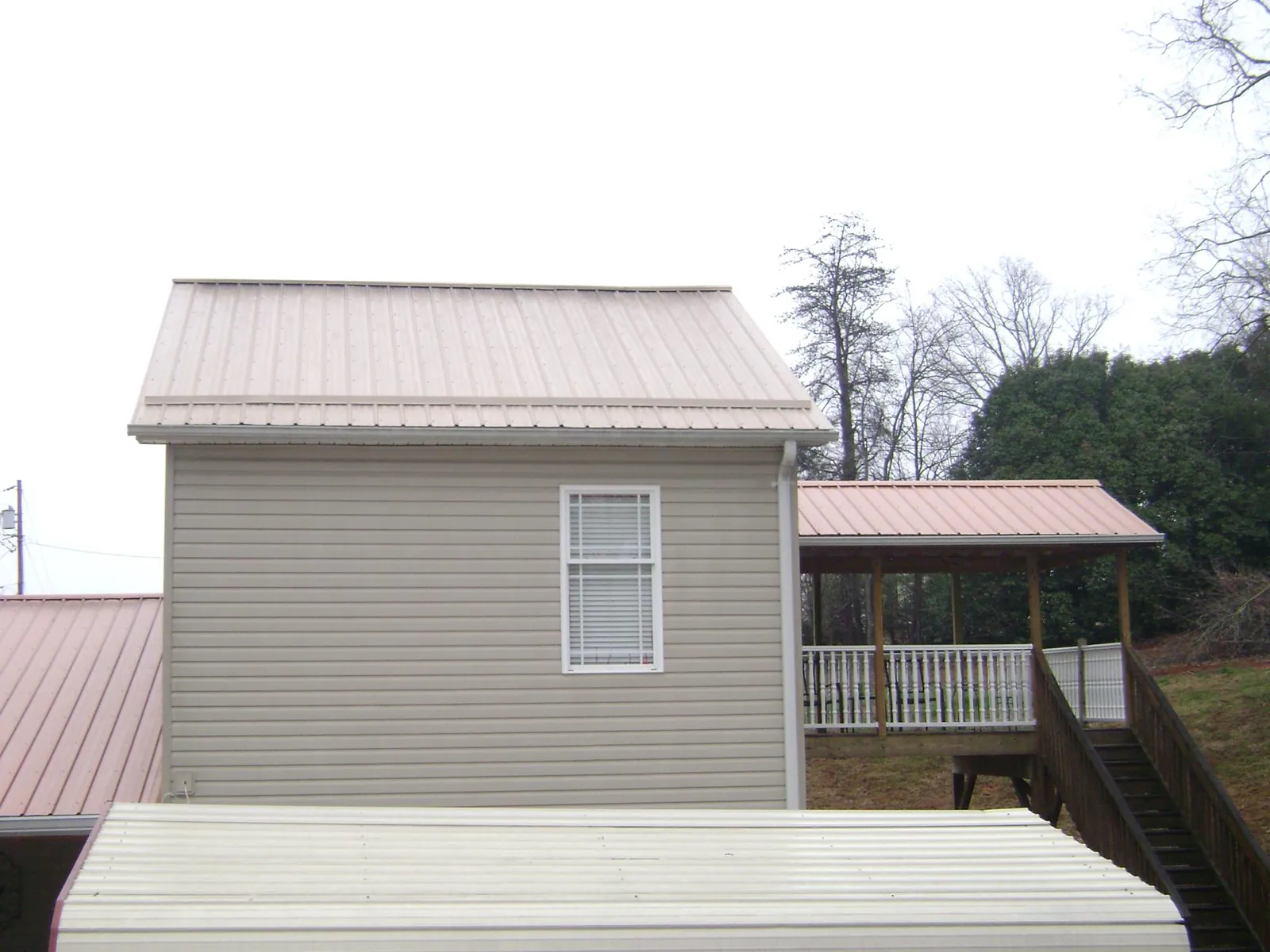 Tan metal roofs on a two story addition and attached porch, from a Roof Replacement job in Pinola
